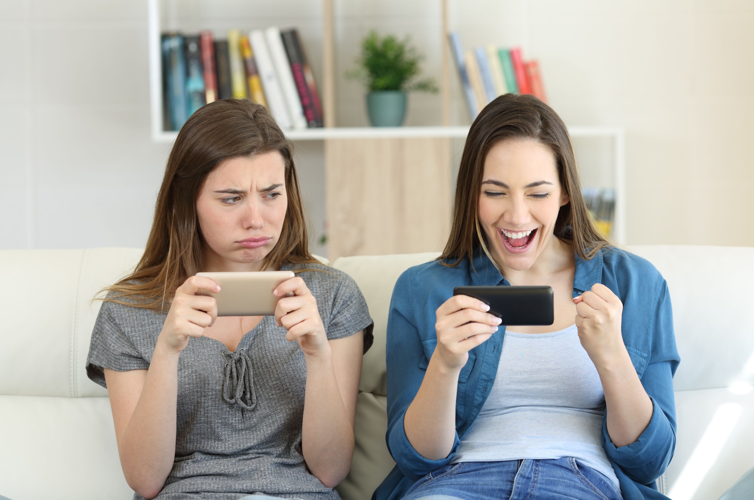 one girl looking envious at the delighted girl next to her on the sofa